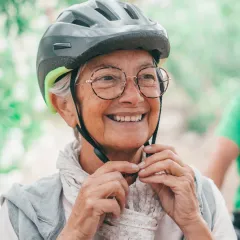 Smiling woman putting on a bike helmet outdoors (actor portrayal)