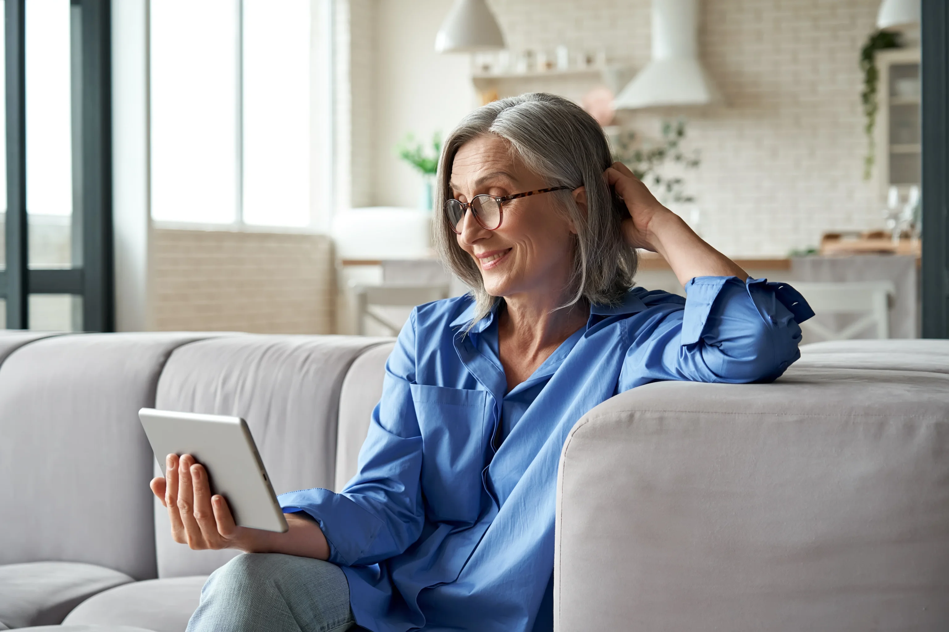 Smiling woman relaxing on a couch at home with a tablet
